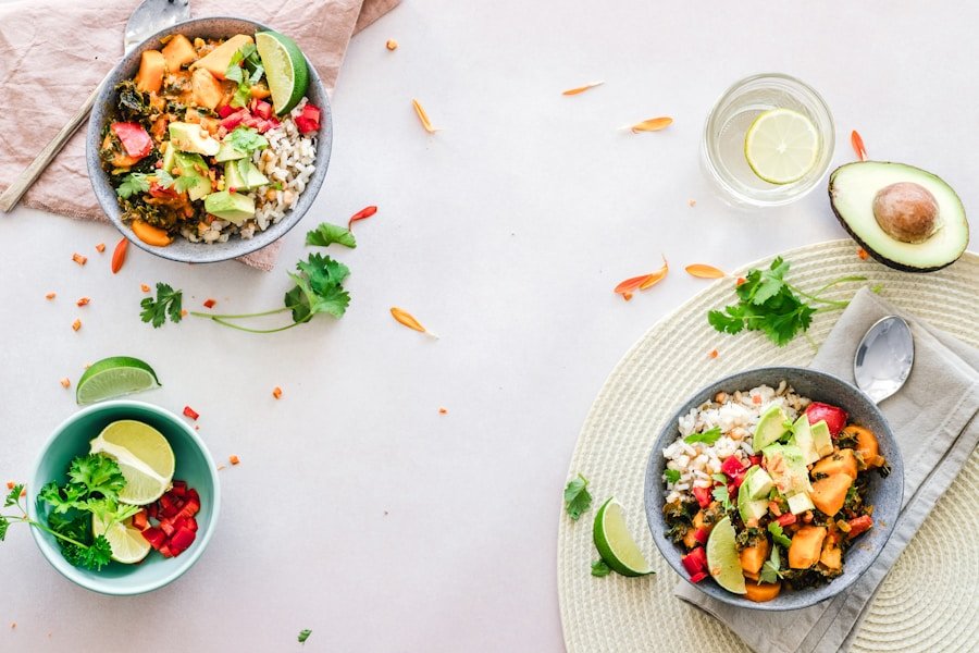 Two bowls of rice with vegetables and avocado on a table, alongside a blue bowl with diced red vegetables, a glass of water with lemon, and scattered greens and lime slices.