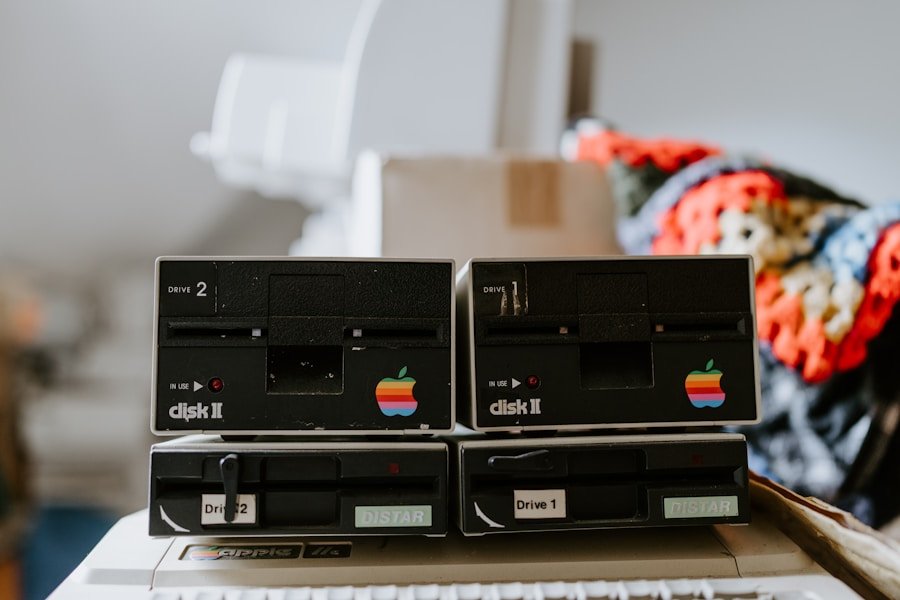 Close-up of two vintage Apple Disk II drives with rainbow apple logos, labeled "Drive 1" and "Drive 2," in a cluttered environment.